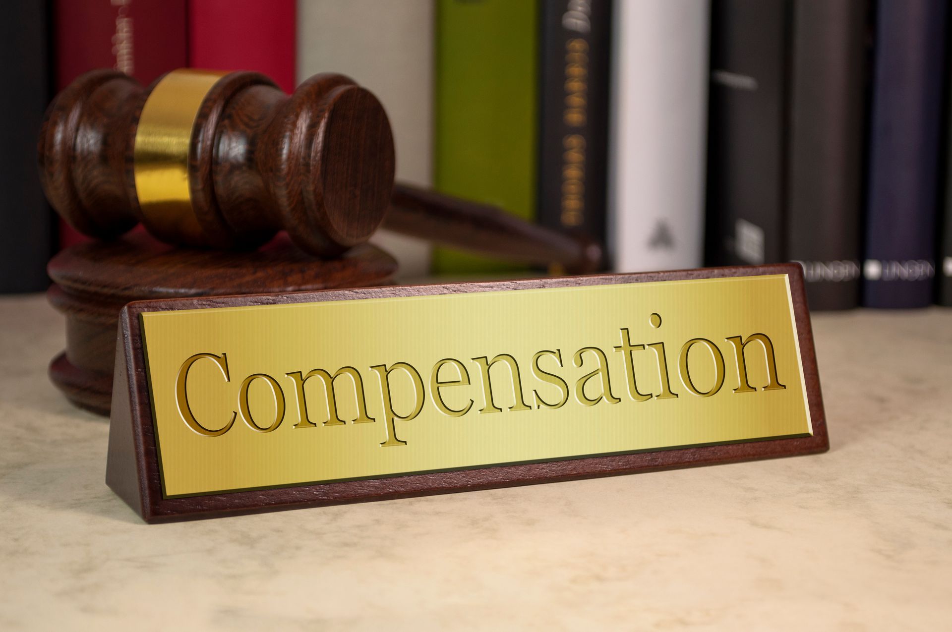 Wooden desk with a plaque labeled “Compensation” and a judge's gavel. Wooden desk with a plaque labeled “Compensation” and a judge's gavel.