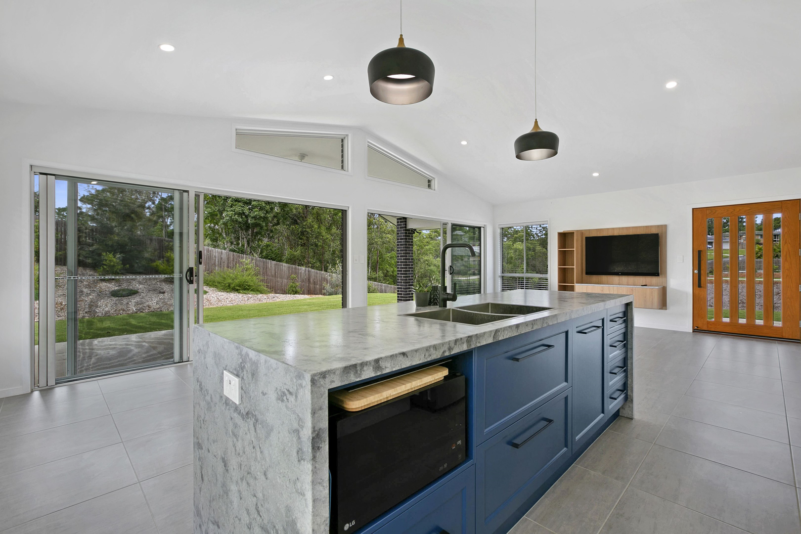 Modern kitchen with a blue island, marble countertop, and sliding glass doors to a backyard. — Morrison Cabinetry in Cedar Pocket, QLD