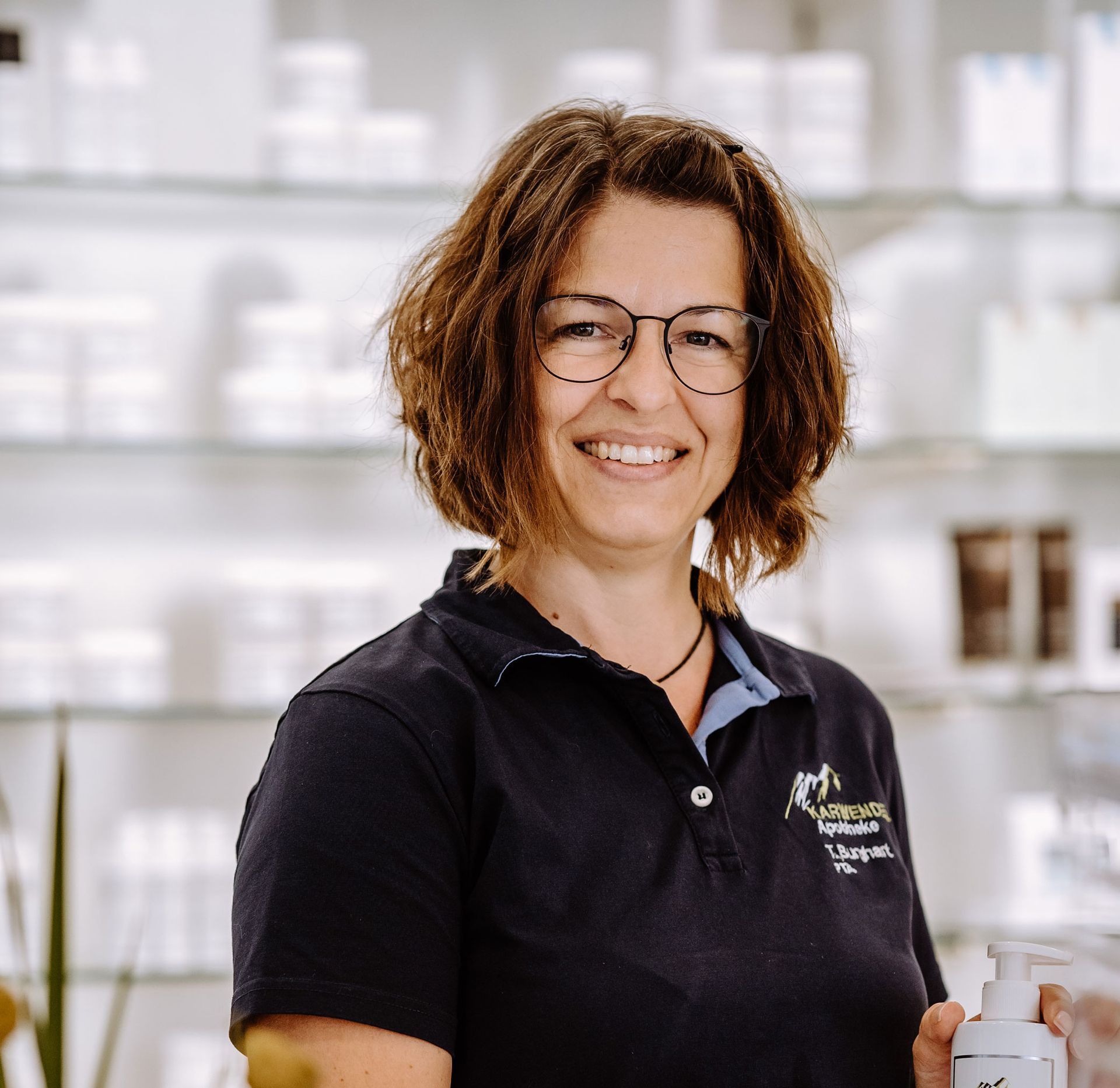 Eine Frau mit Brille und schwarzem Hemd hält eine Flasche Seife.