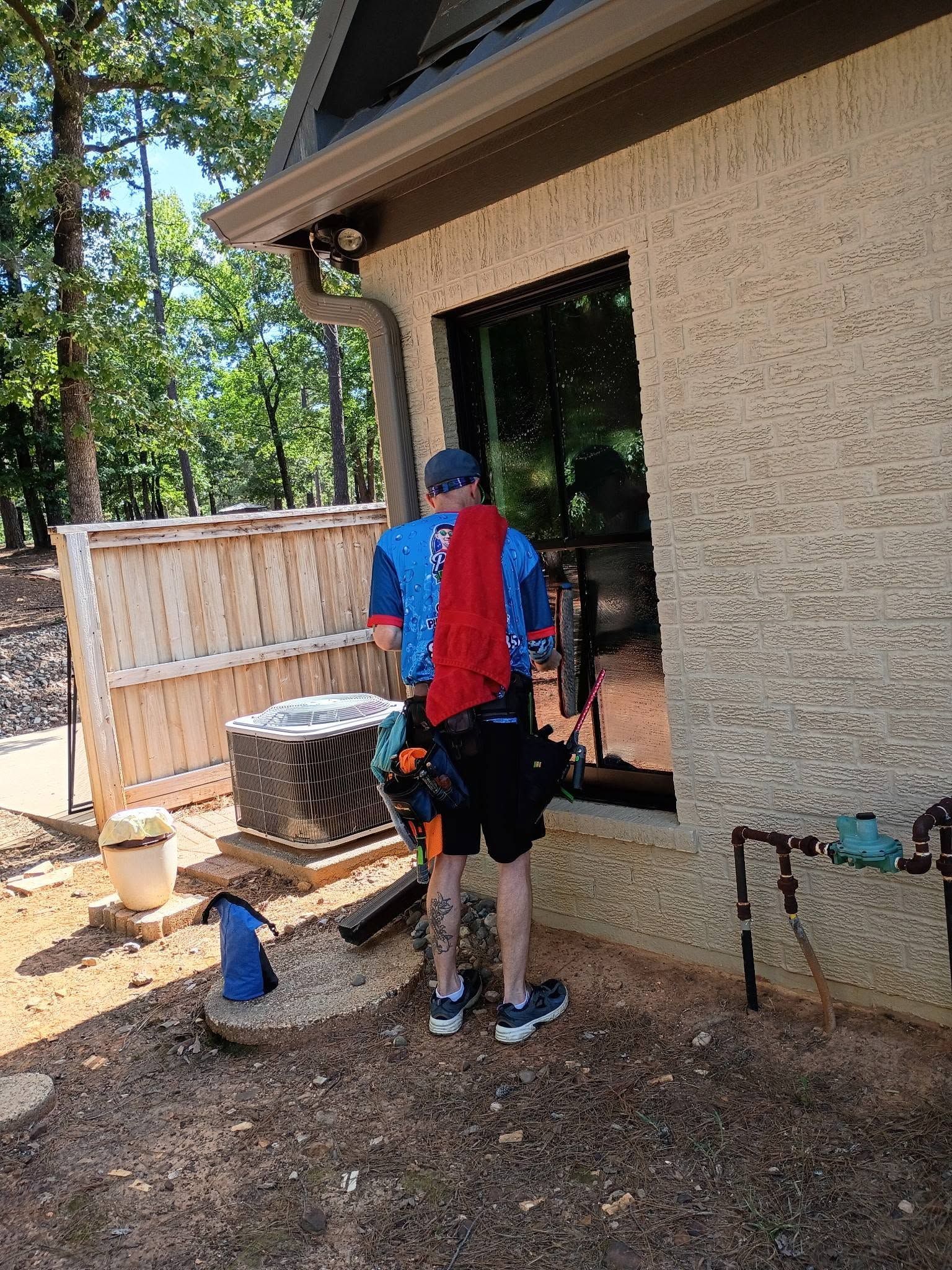 Person in blue and red shirt standing by a window during outdoor home repairs.