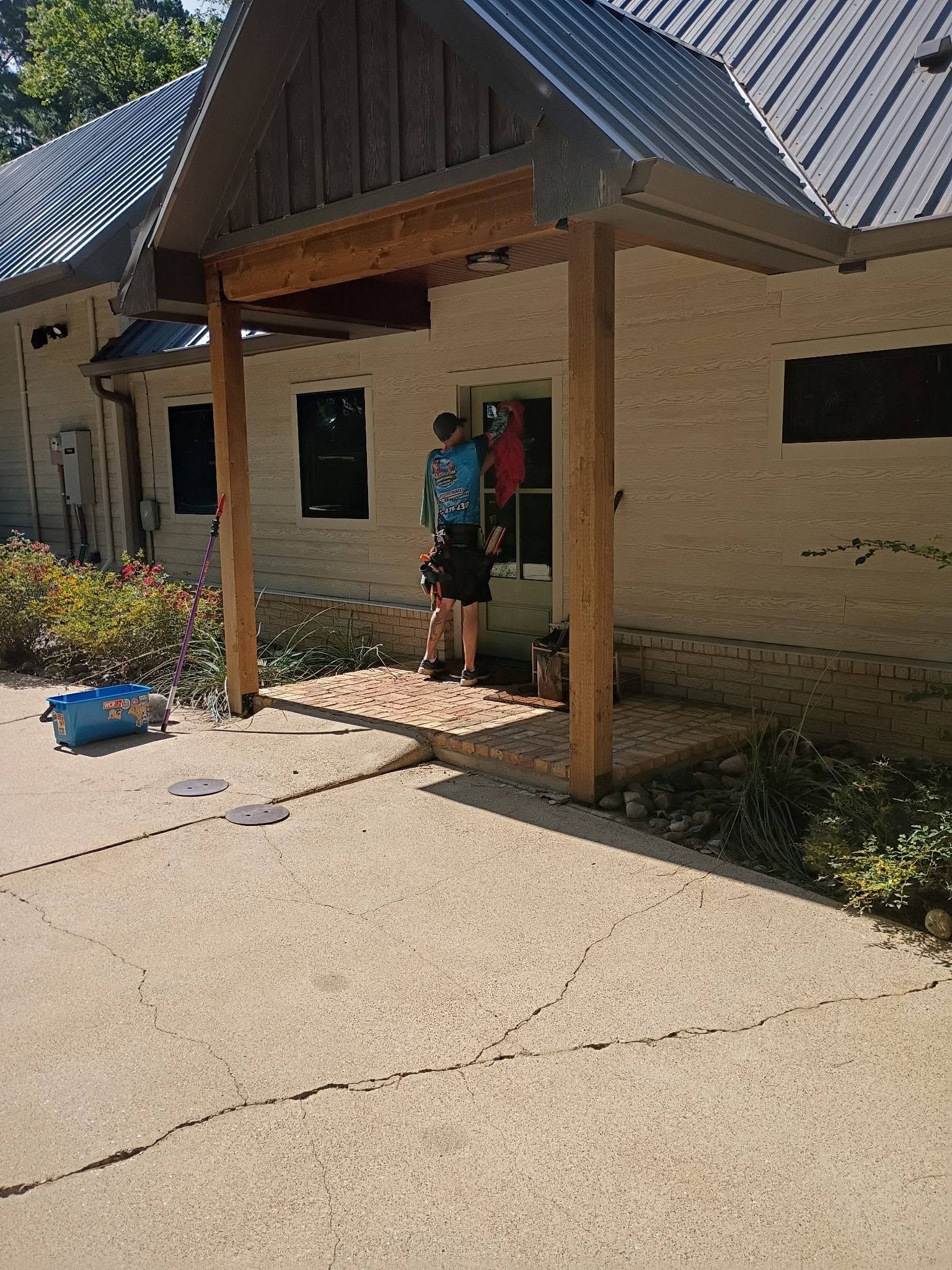 Person standing at a building entrance with wooden posts and a tiled roof, holding items near the doorway.