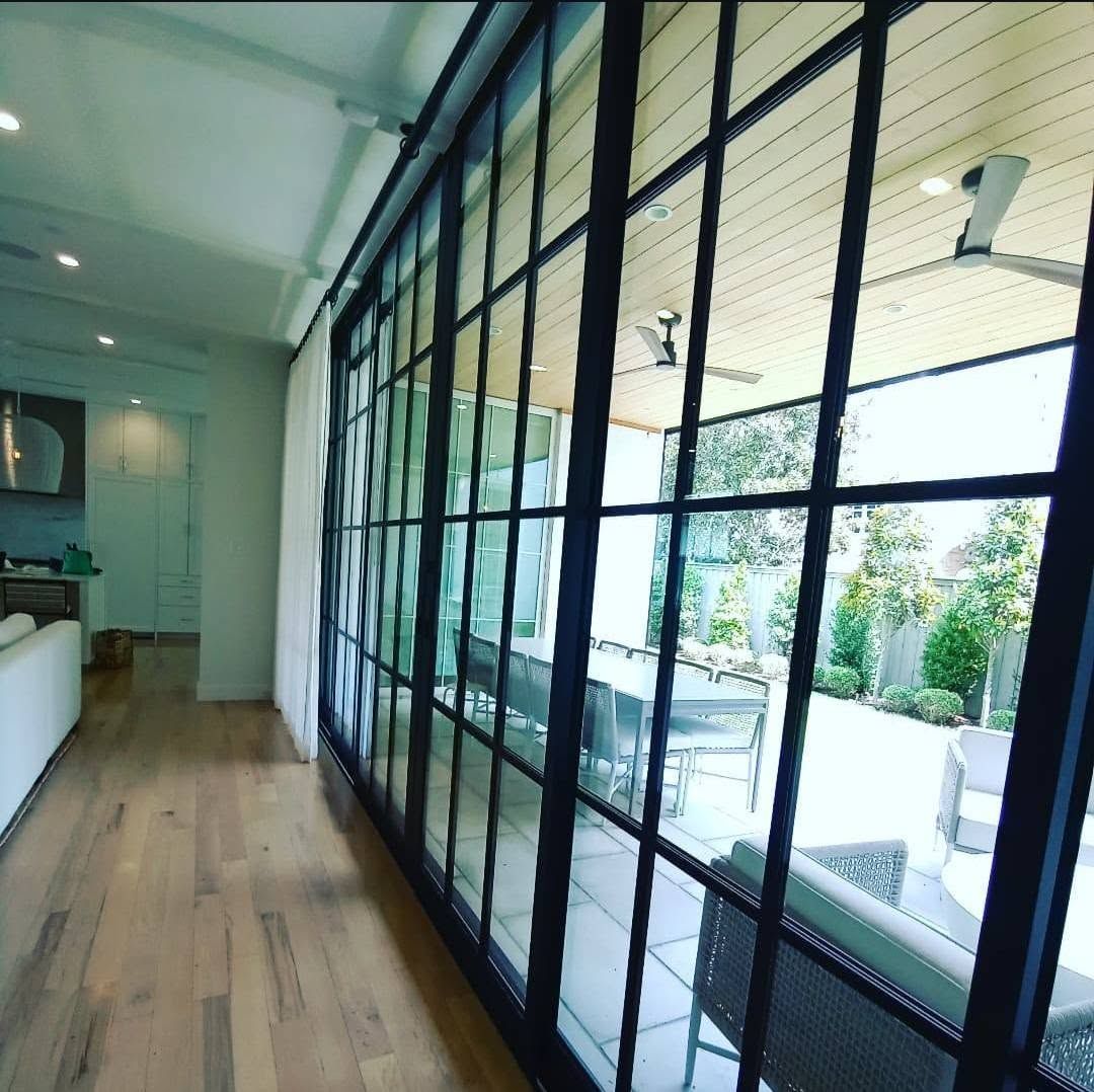 Bright hallway with wood floors and black-framed glass walls opening to a courtyard.