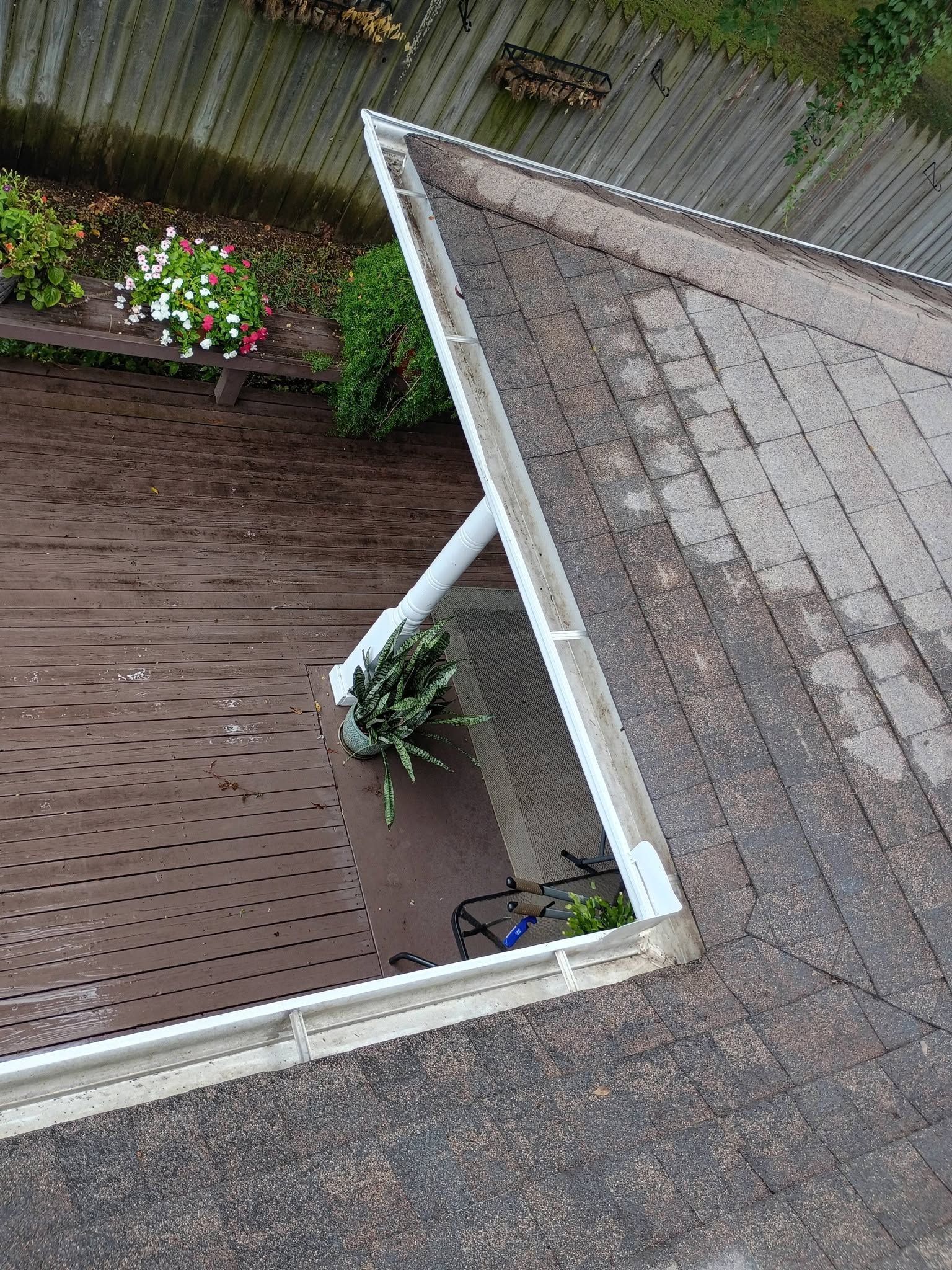Tilted rooftop and white gutter over a brown wooden deck with potted plants.