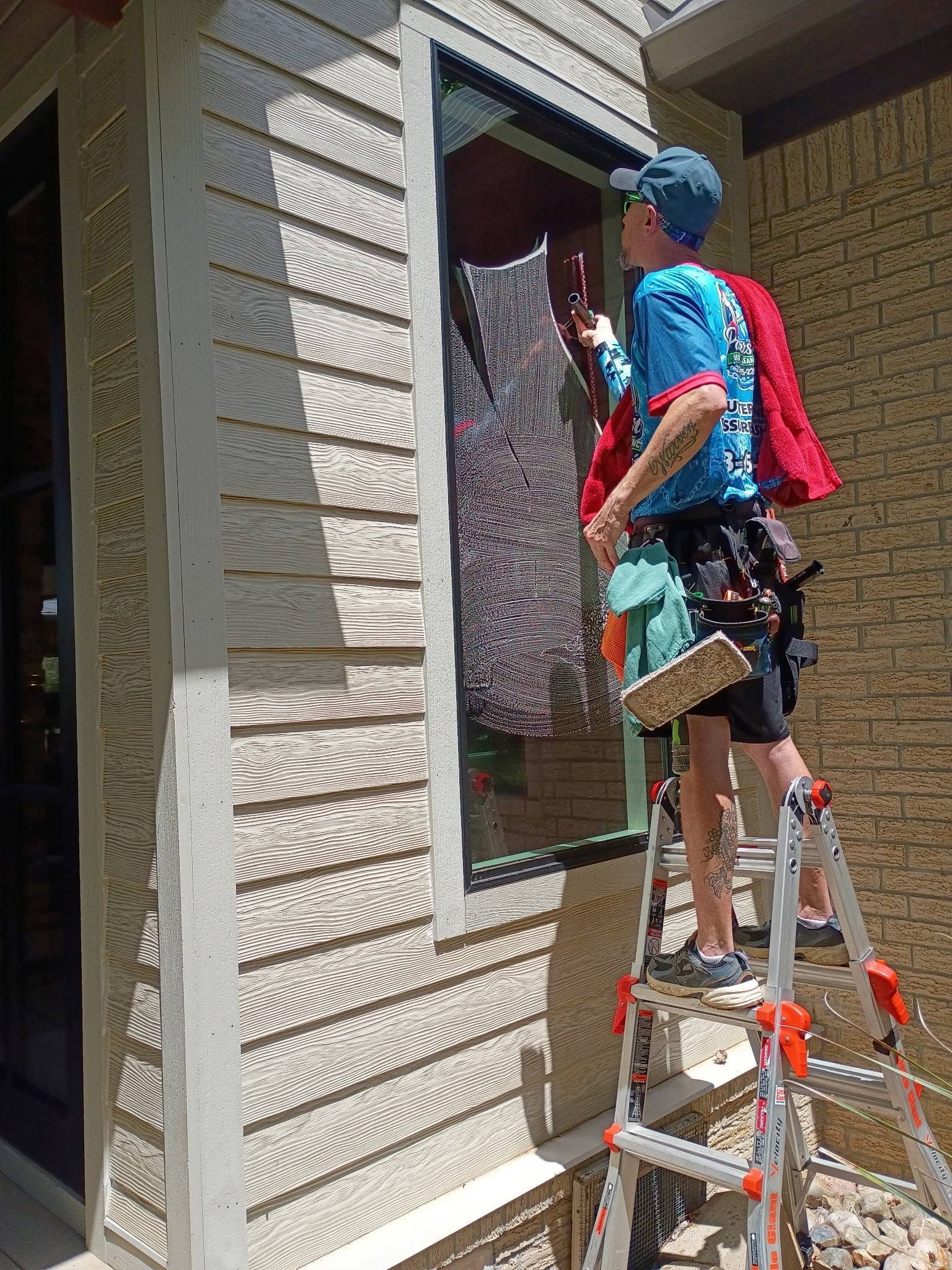 Person on a ladder painting a house window frame red