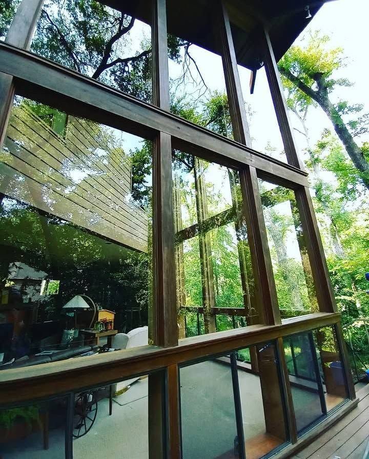Glass-walled building walkway with wooden frames reflecting trees outside