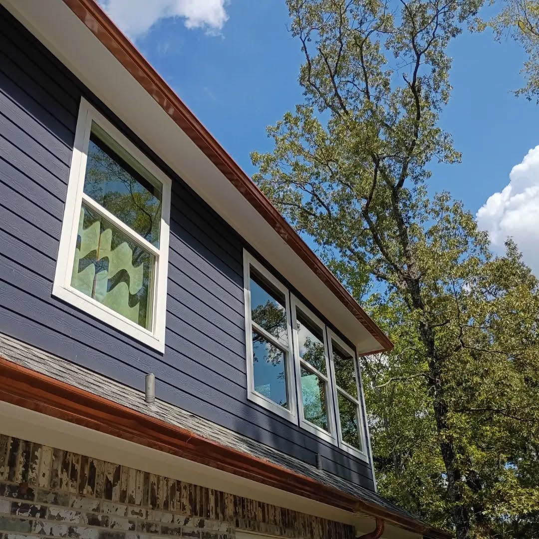 Blue house exterior with white-trimmed windows and a tall tree against a sunny sky
