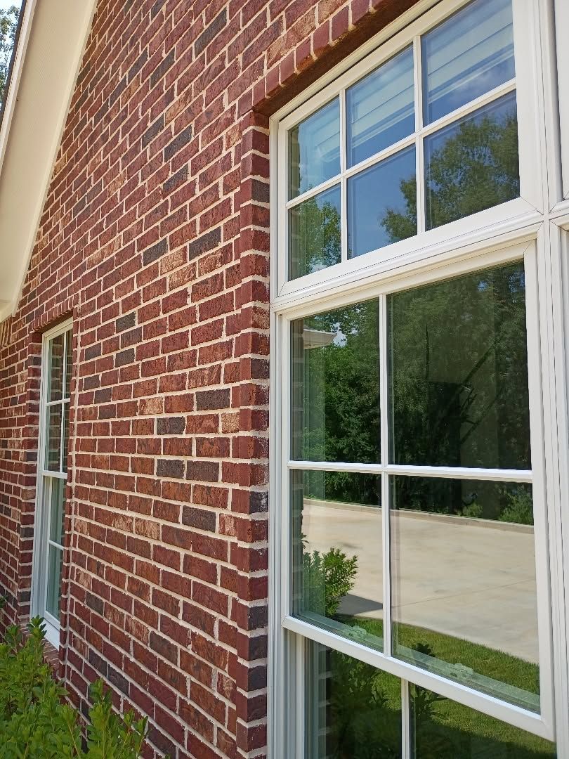 Red brick building wall with white-framed window reflecting trees and a driveway