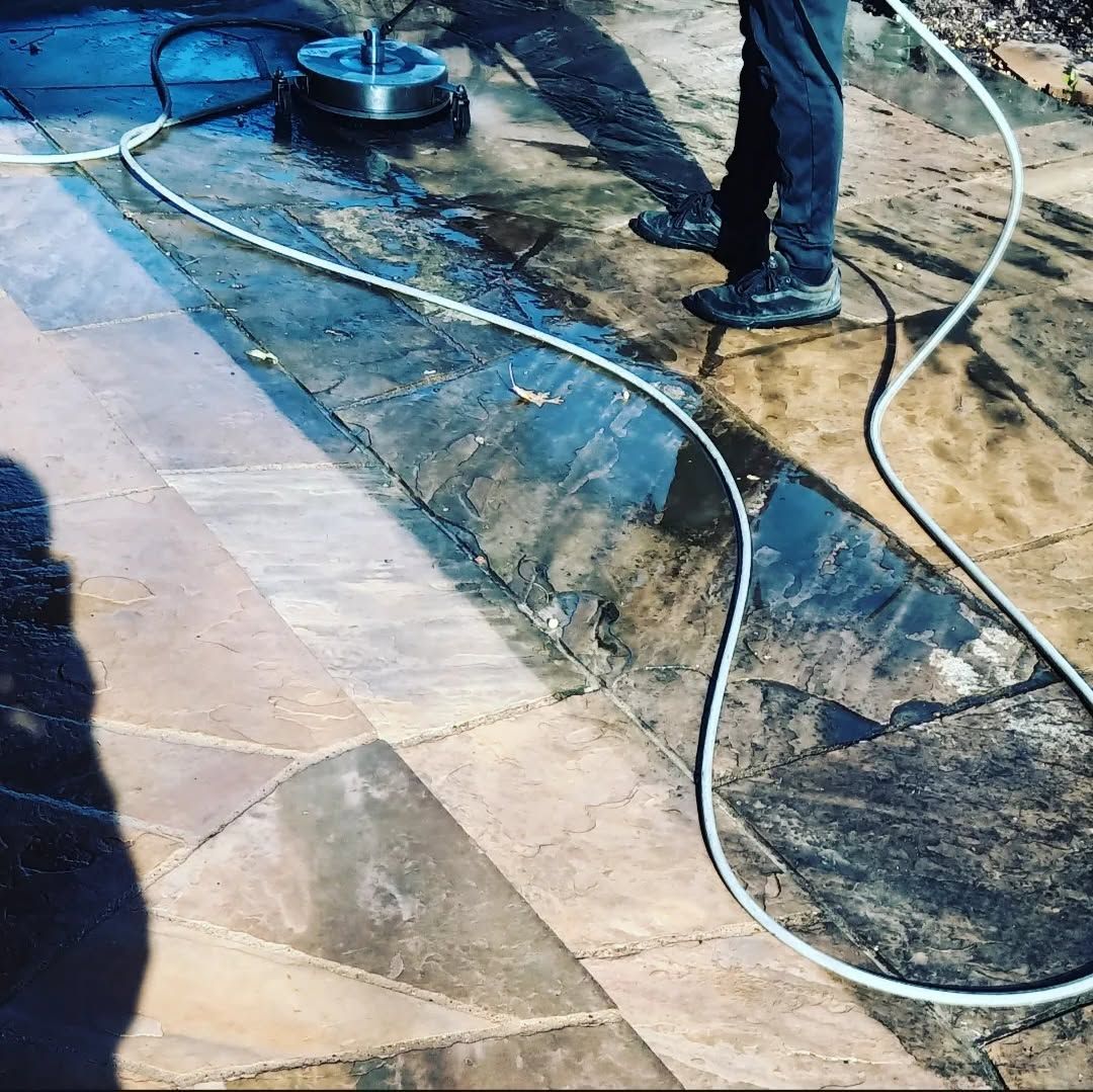 Two workers pressure-washing a stone patio with hoses and a floor scrubber.