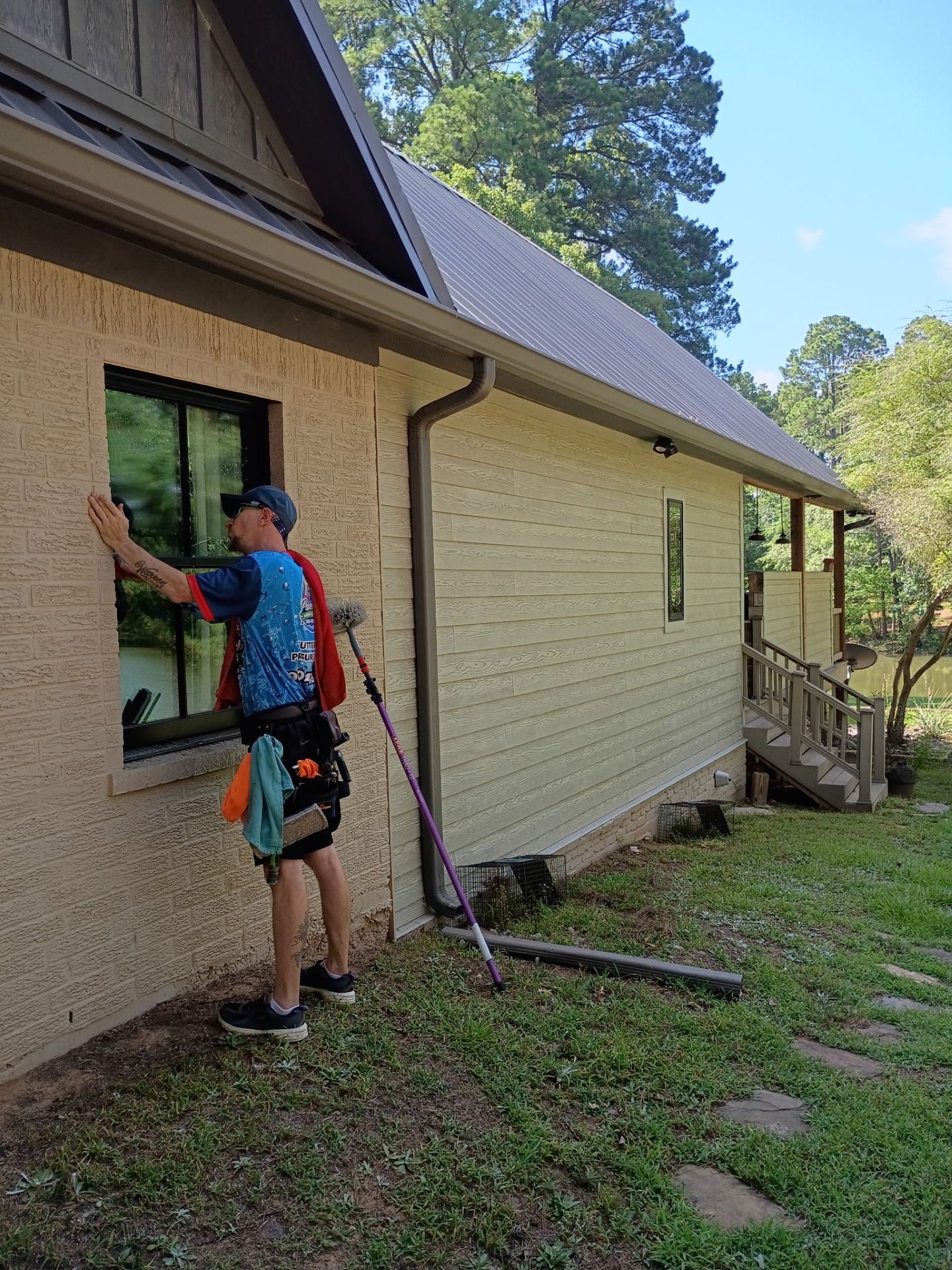 Person working on exterior wall of a tan house with a paint roller on a sunny day