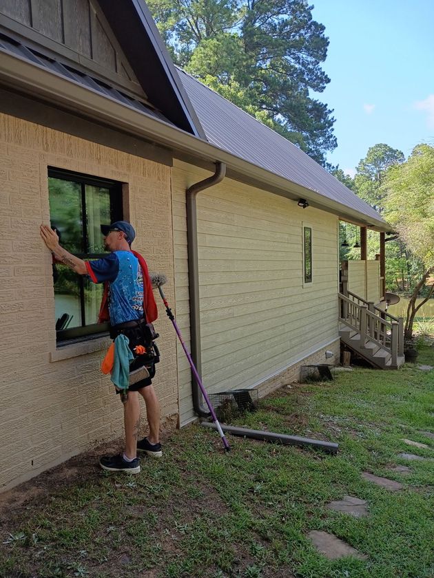 Person working on exterior wall of a tan house with a paint roller on a sunny day