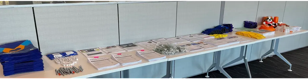 Long table with neatly arranged papers, trays, and small items in a classroom or event display.