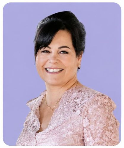 Smiling woman in a light pink lace top against a lavender background