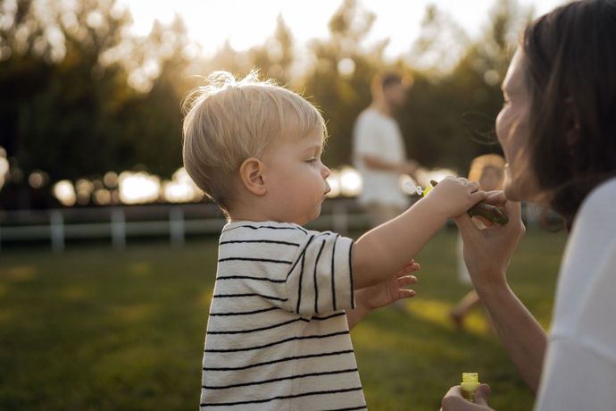 Child in striped shirt reaching for a snack from an adult outdoors at sunset