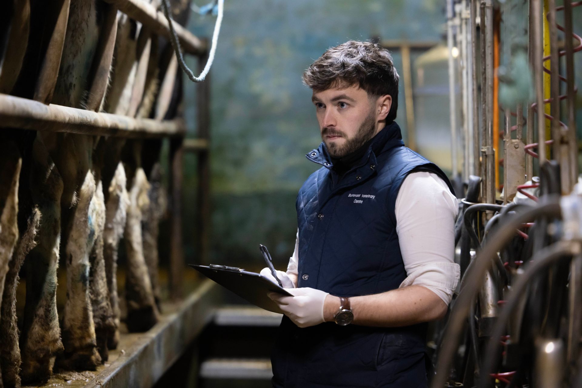 Man holding a clipboard in a fish processing facility, inspecting rows of hanging fish among metal racks.