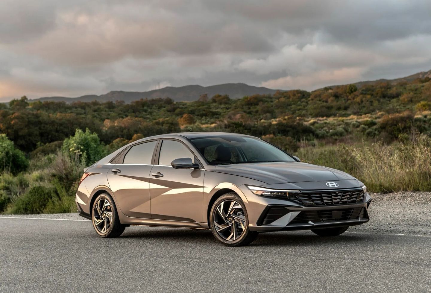 A silver Hyundai Elantra sedan parked on a road with a mountainous backdrop.