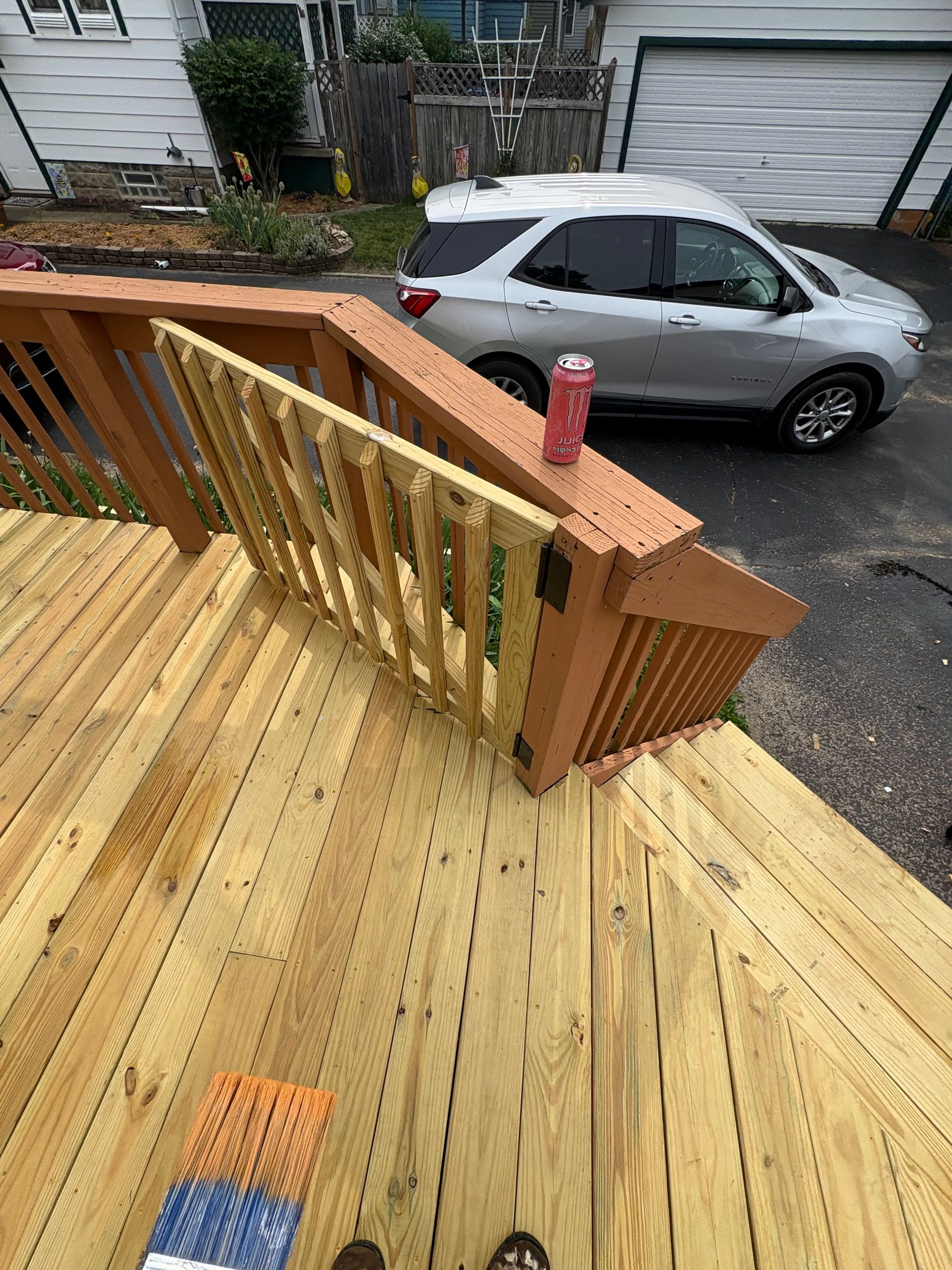 Wooden deck stairs with a red railing above a parked silver car on a residential street.