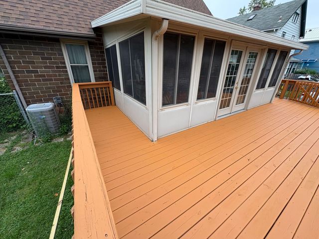 Orange deck wraps around a screened porch beside a brick house and grassy yard