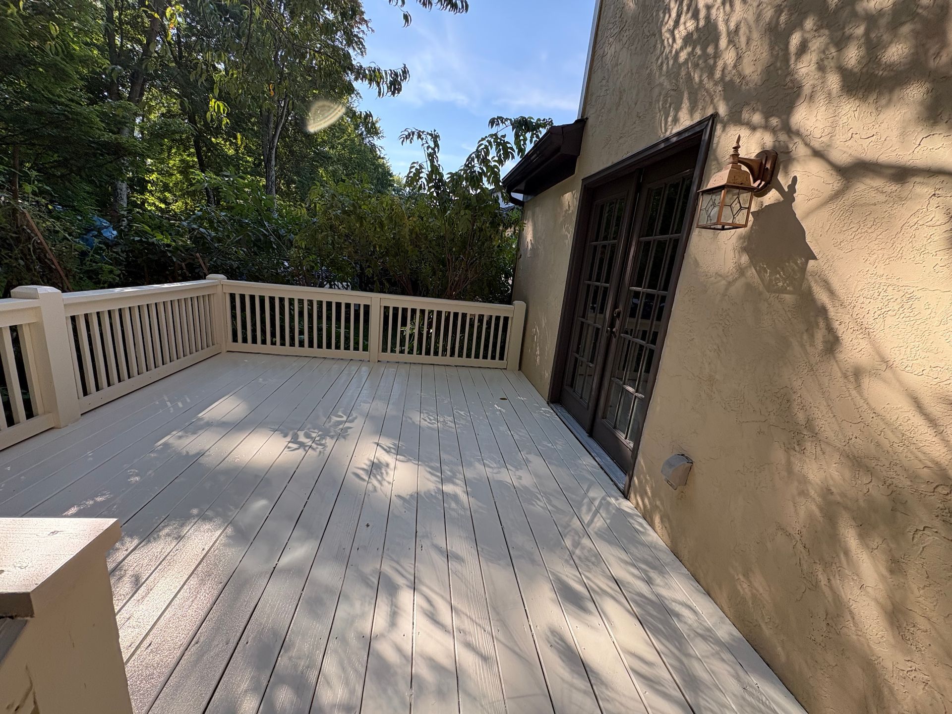 Sunlit wooden deck with white railing beside a tan stucco house and sliding door