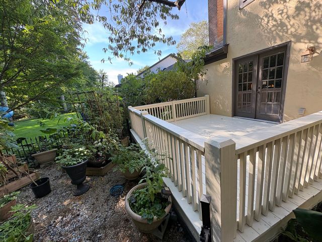 Wooden deck beside a house, with potted plants and leafy garden greenery.
