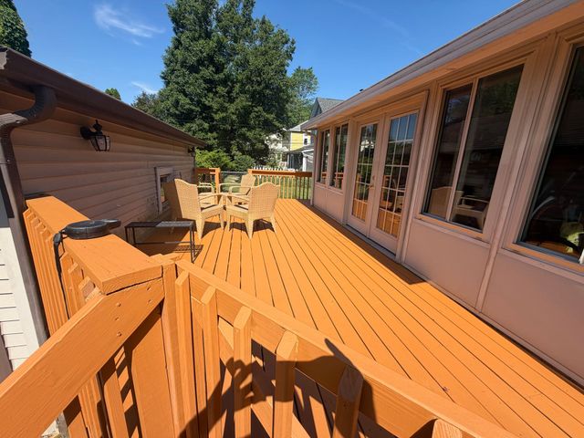 Wooden backyard deck with patio chairs beside a house under a blue sky