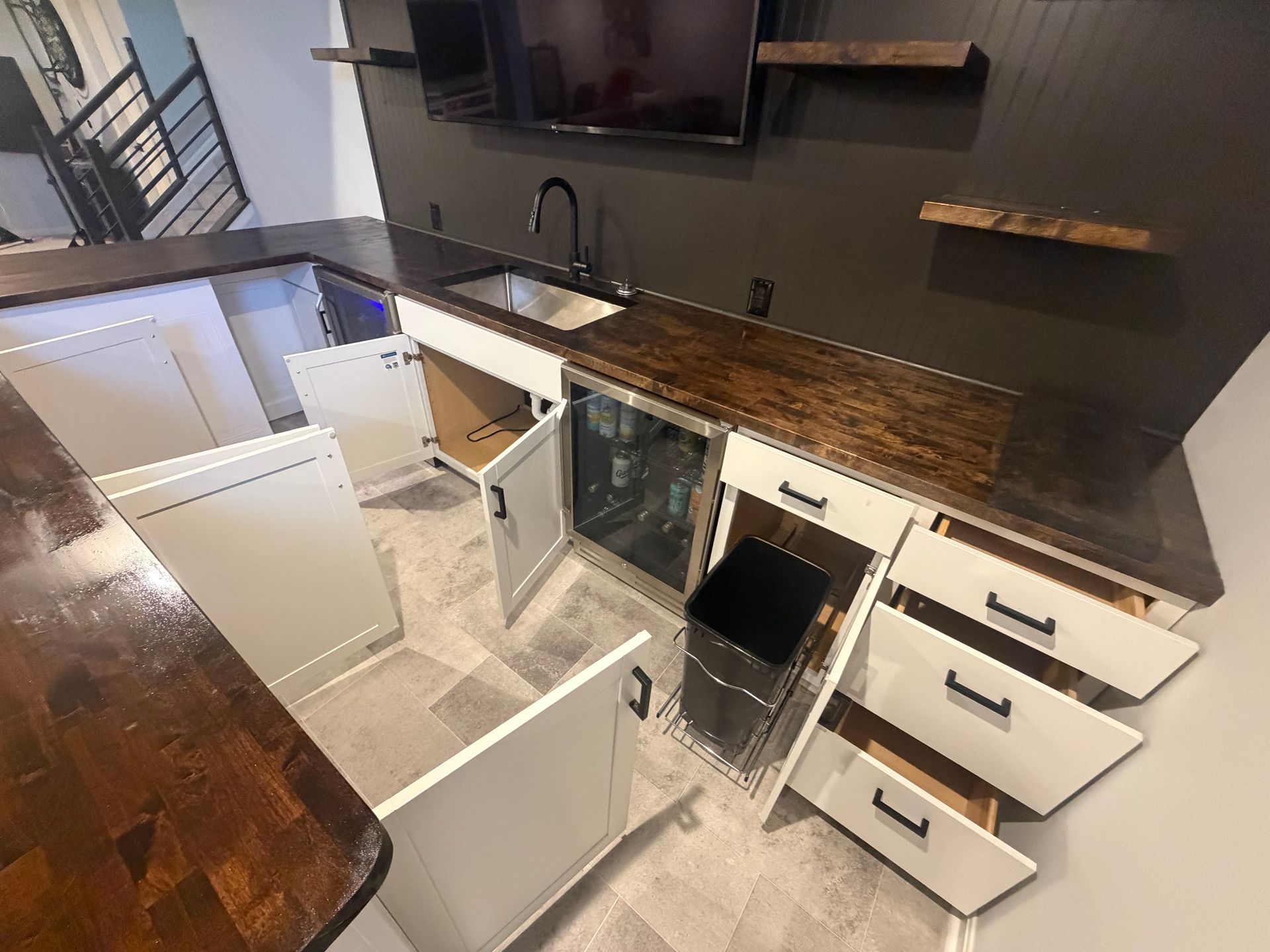 Modern kitchen with open cabinets, dark wood countertop, and drawers pulled out during renovation.