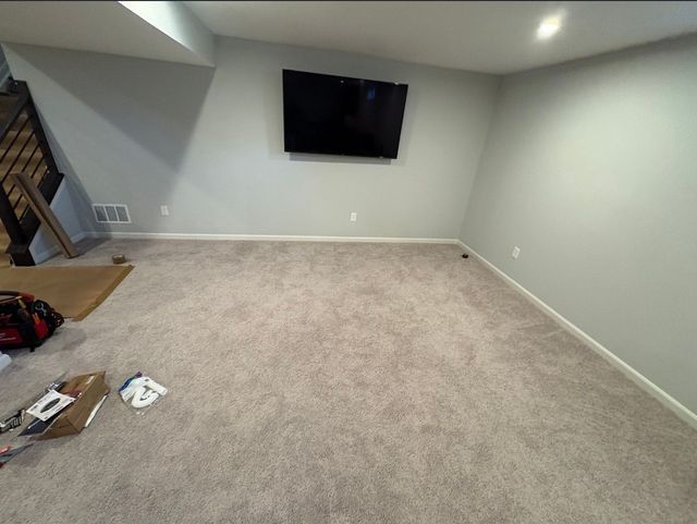 Empty carpeted living room with wall-mounted TV and stairs on the left