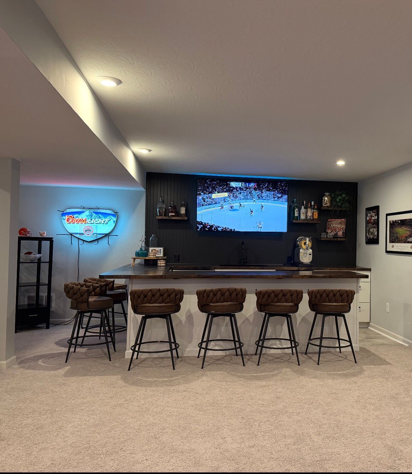 Basement bar with five stools, neon sign, and TV showing a hockey game