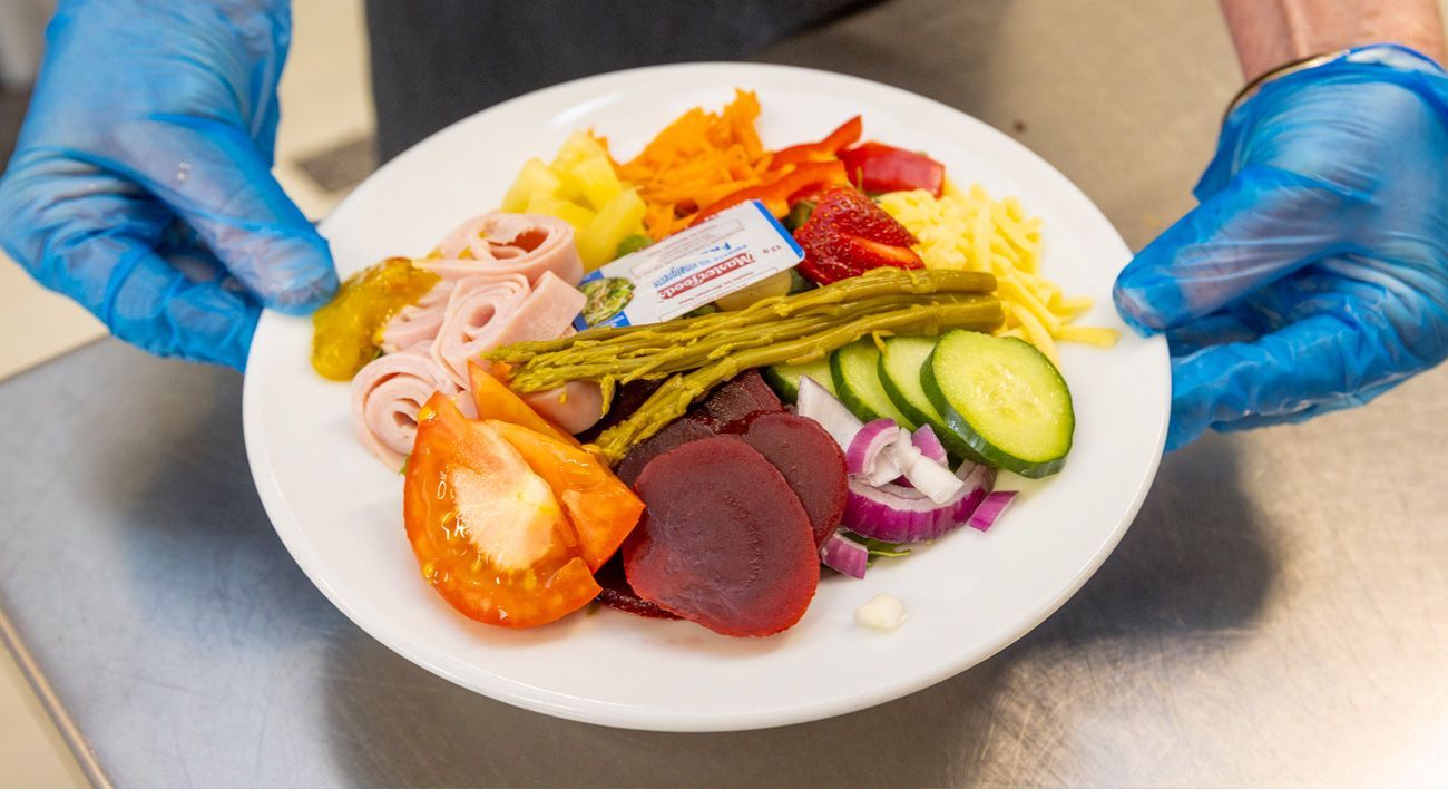 A person wearing blue gloves is holding a plate of food.