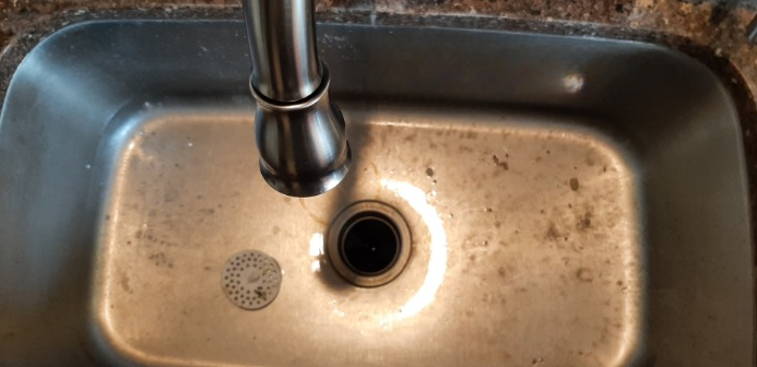 A dirty kitchen sink with a faucet coming out of it.
