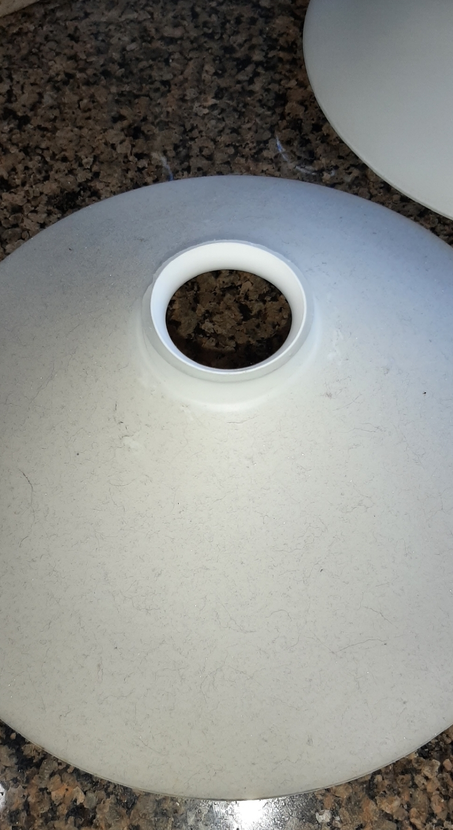 A white glass shade with a hole in the middle is sitting on a granite counter.