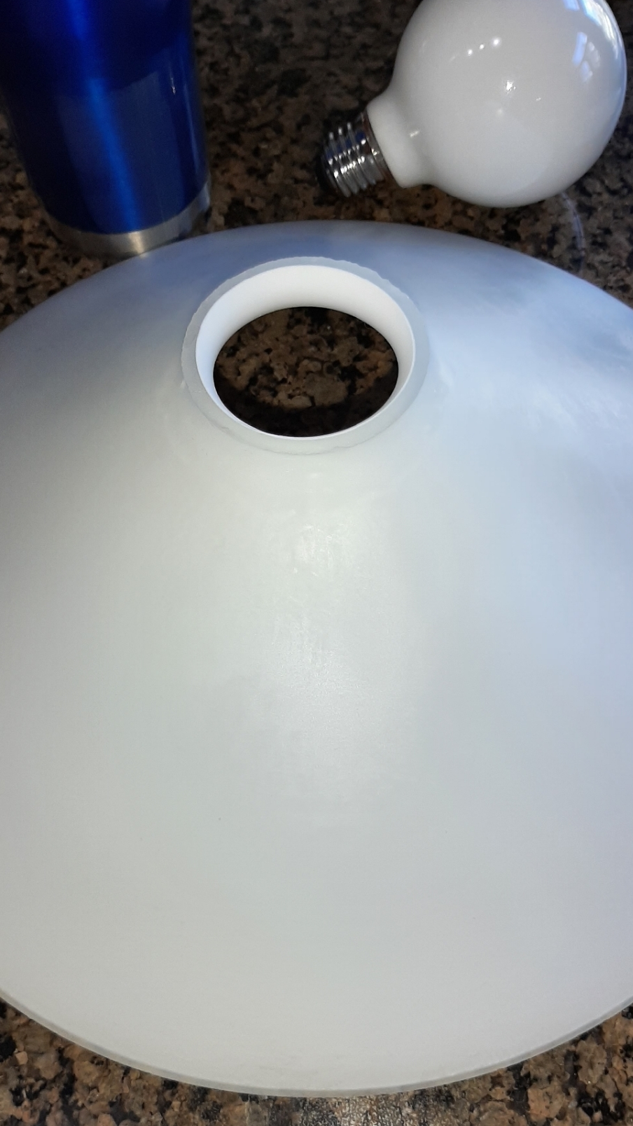A white light shade with a hole in the middle is sitting on a counter next to a light bulb.