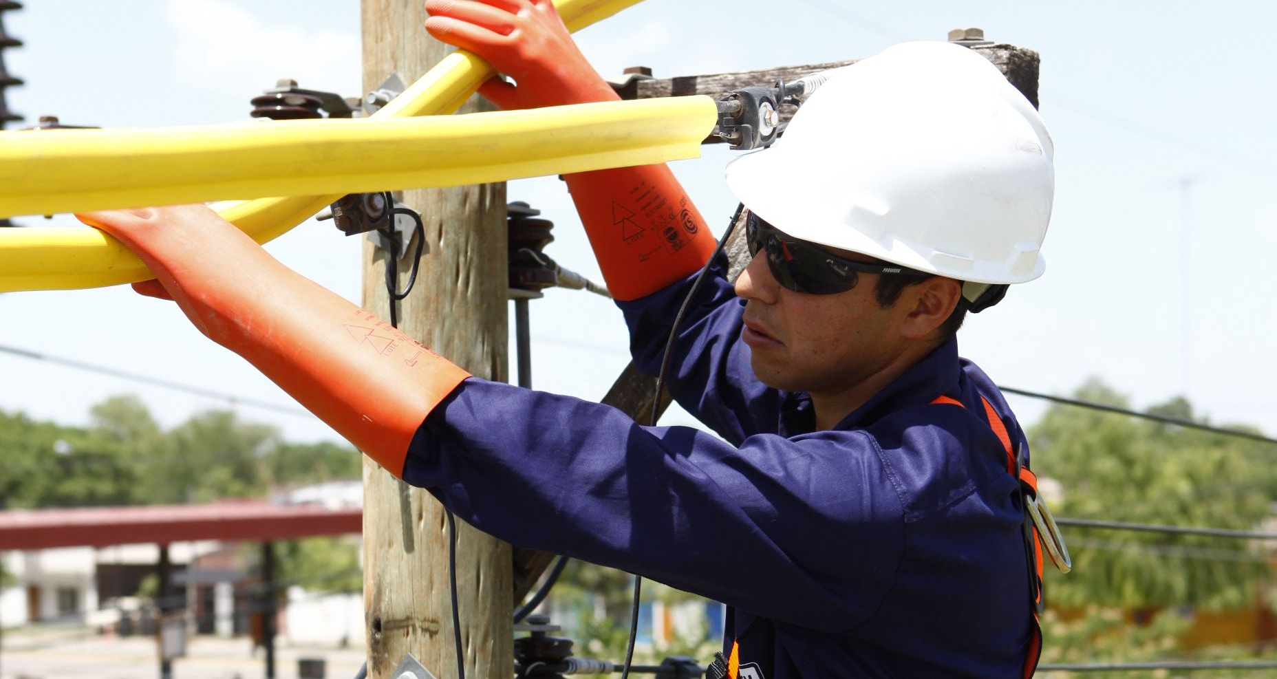 Liniero en un poste de servicios públicos, con equipo de seguridad y trabajando en líneas eléctricas.