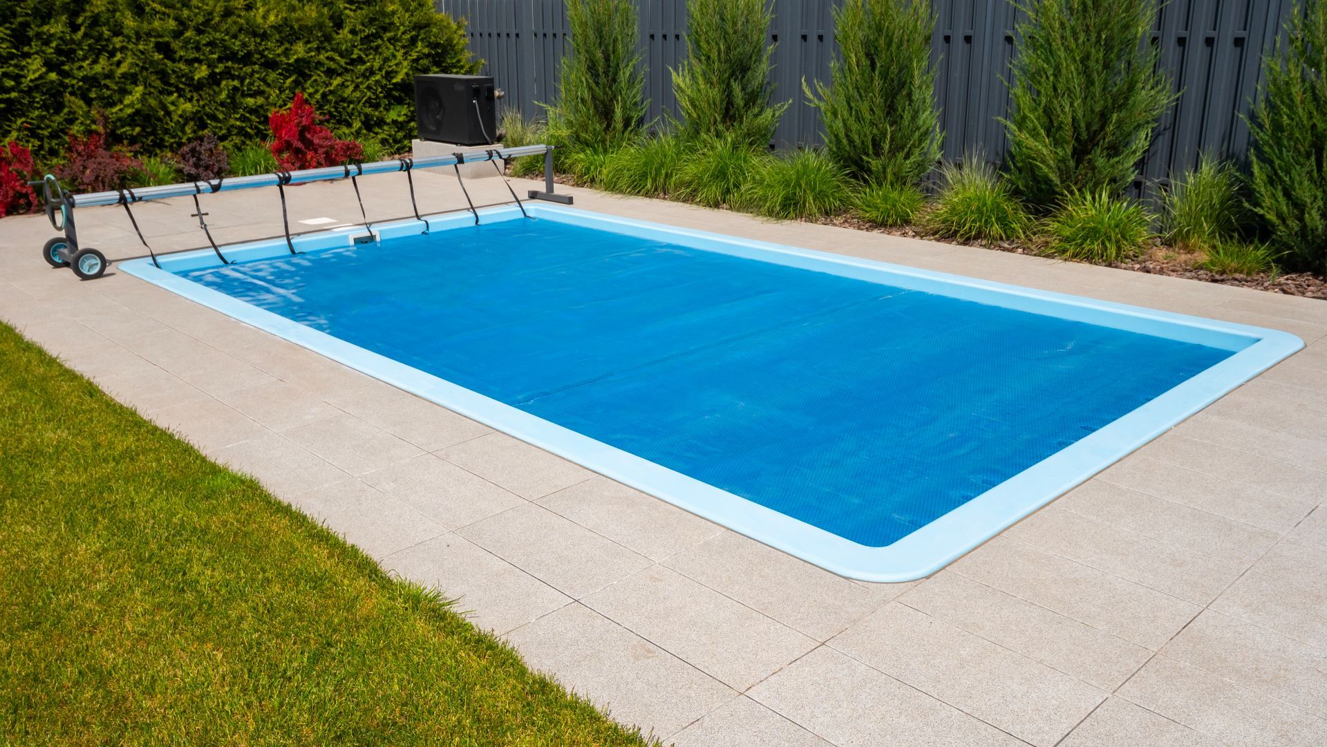Rectangular backyard swimming pool with blue water, white coping, and garden fencing