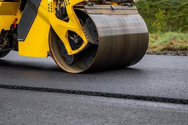 Yellow road roller compacting fresh asphalt on a road surface