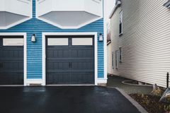 Blue and white garage doors beside a narrow side path and white siding, on a wet driveway