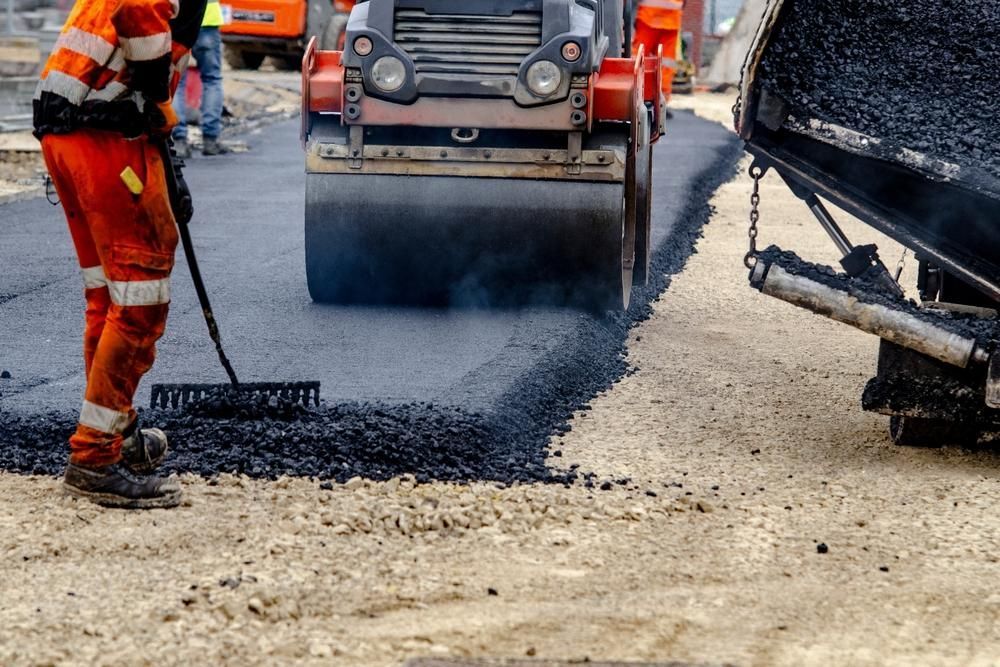 Road crew spreading fresh asphalt beside a paving machine and truck