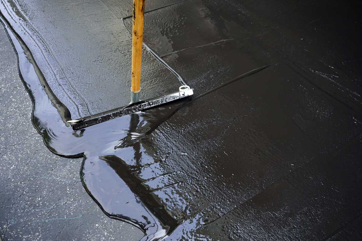 Person smoothing black wet asphalt with a trowel near a yellow pole