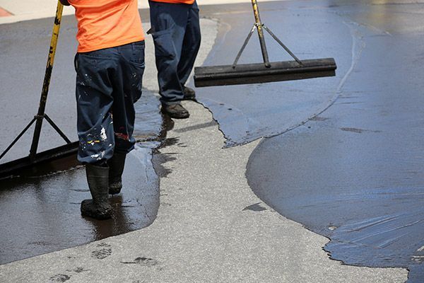 Workers smoothing wet concrete with squeegees on a driveway or sidewalk