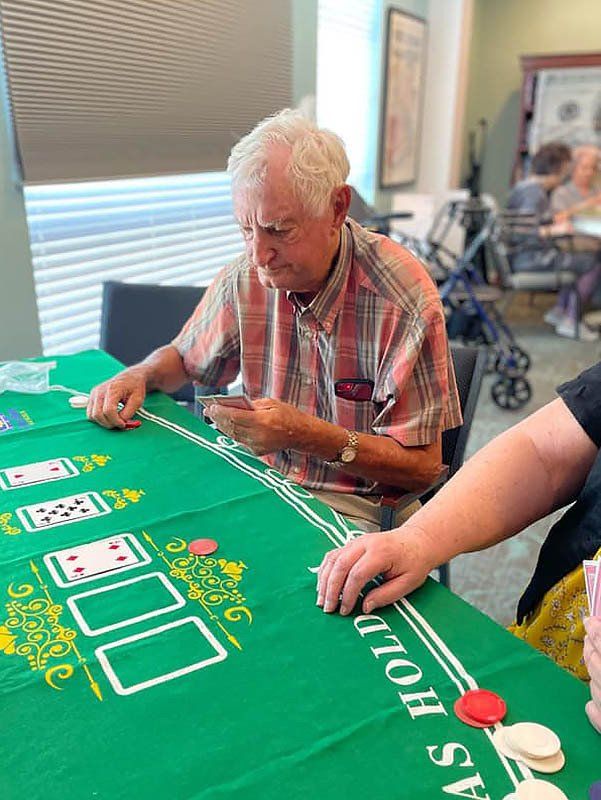 Man playing cards at a table with green felt. He is looking at his hand; others are at the table.