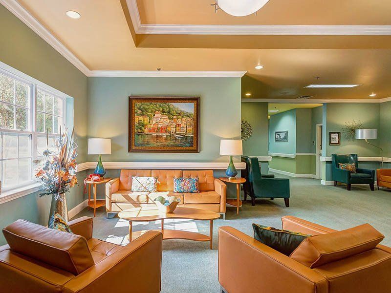 A light-filled living room with leather furniture, lamps, and a painting, in a senior living facility.