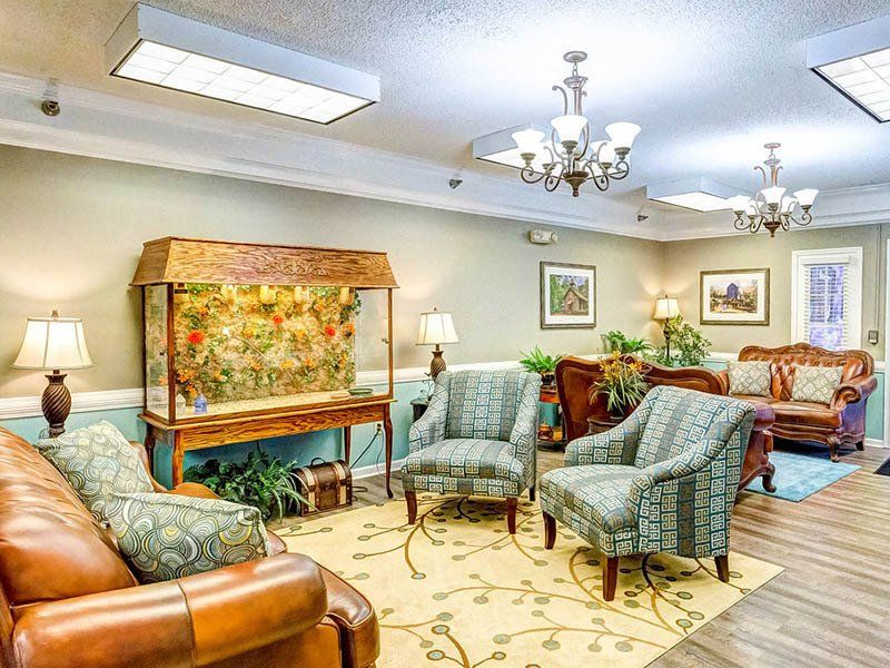 Lounge area with aquarium, patterned chairs, leather sofas, area rug, chandeliers, lamps, and framed art.