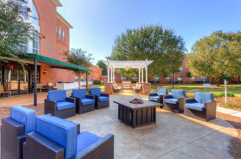 Outdoor patio with blue cushioned seating, a fire pit, and a pergola, next to a brick building on a sunny day.