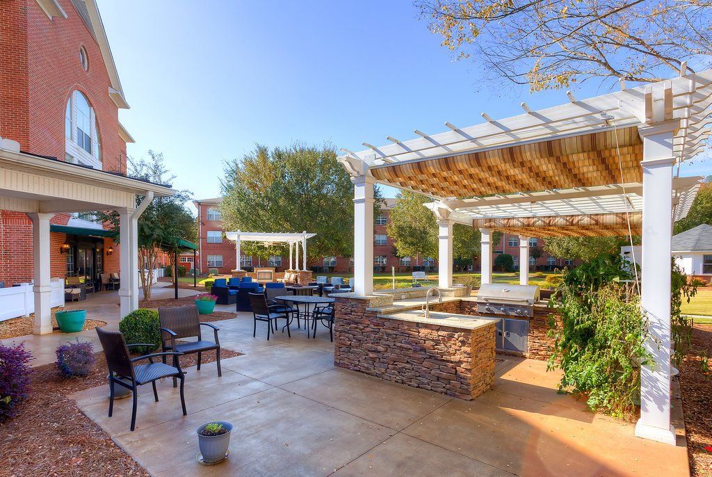 Outdoor patio with pergola, seating, and brick building under a sunny blue sky.