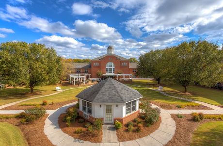 A large red brick building with a white gazebo in front, set in a landscaped yard under a blue sky.