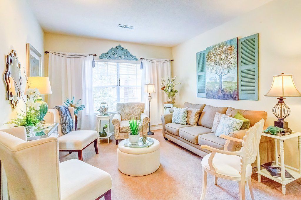 Bright living room with beige furniture, patterned pillows, a large window, and colorful artwork.