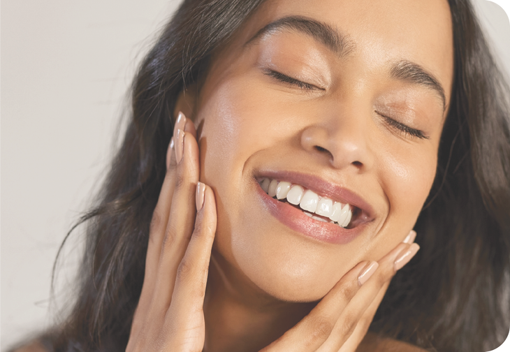 A woman is smiling and touching her face with her hands.