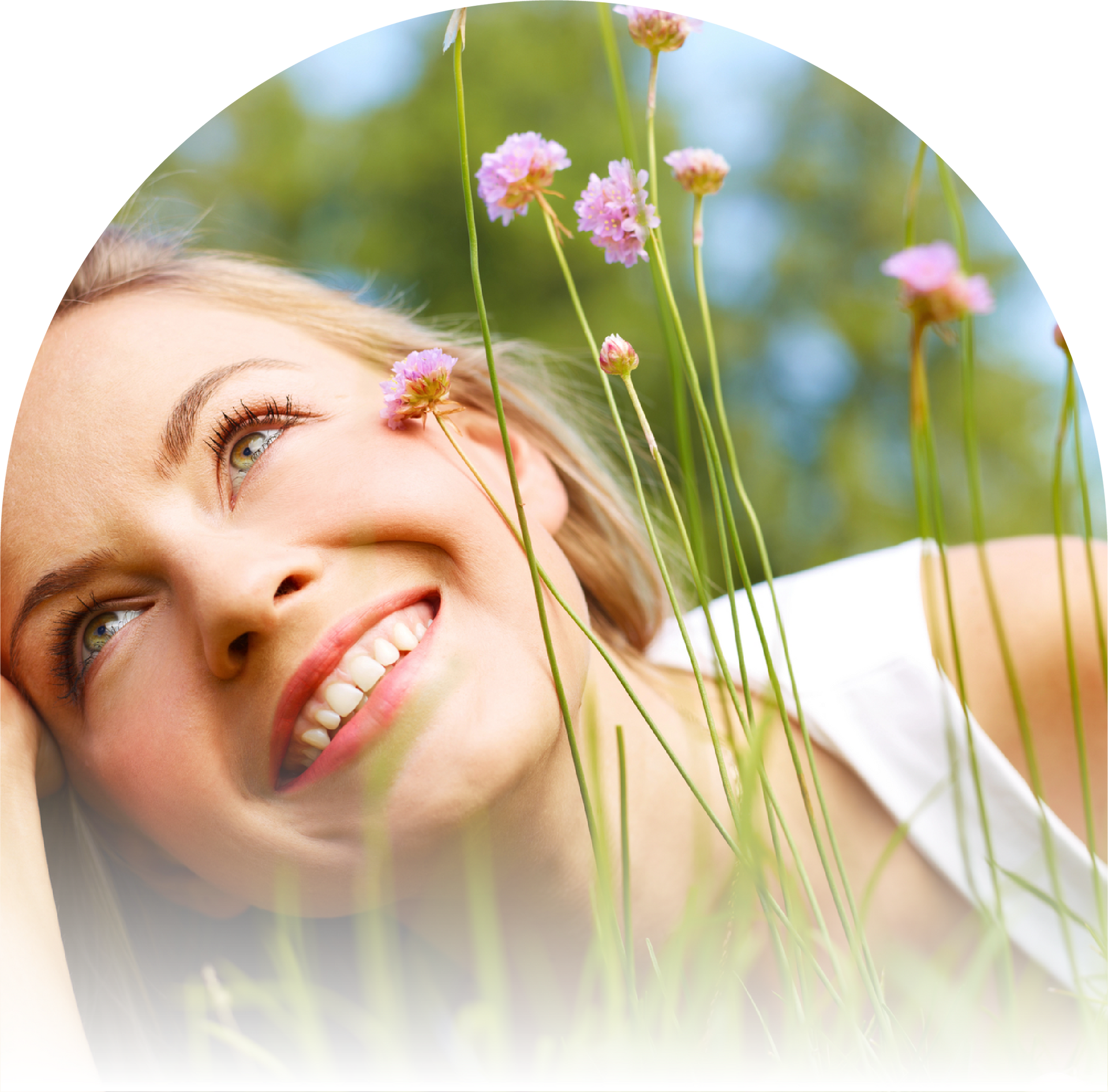 A woman is smiling in the grass with purple flowers