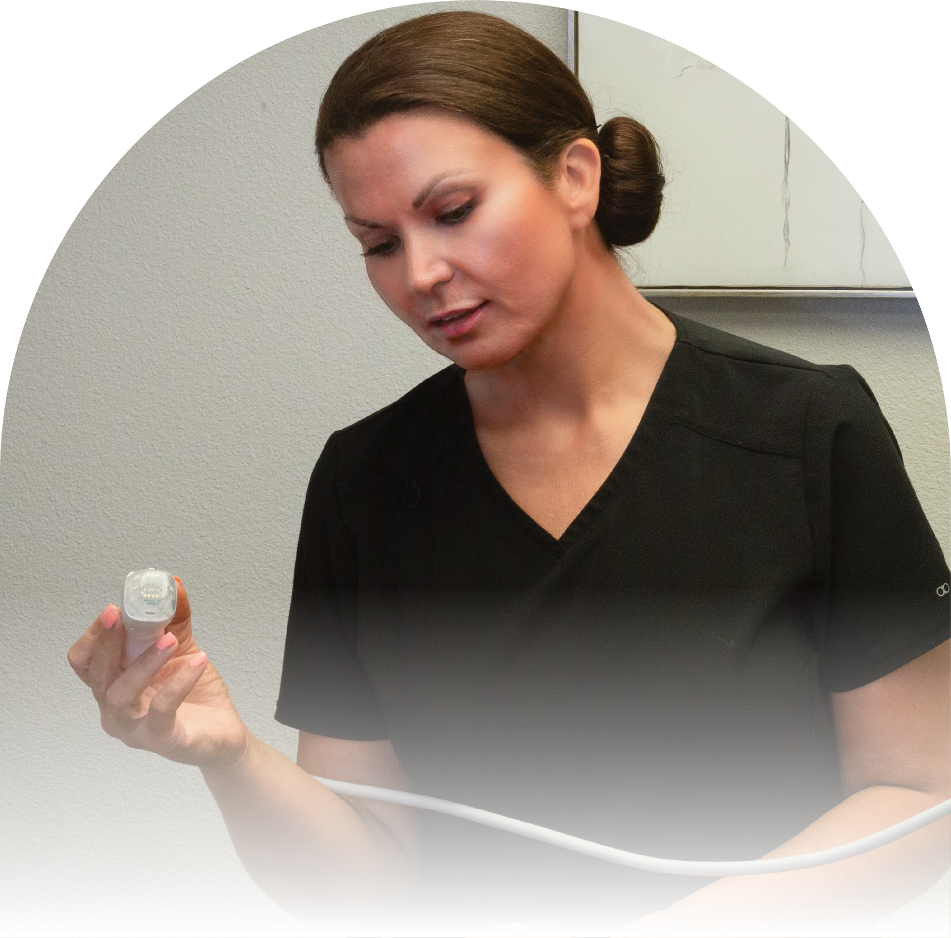 A woman in a black scrub top is holding an aesthetic device.