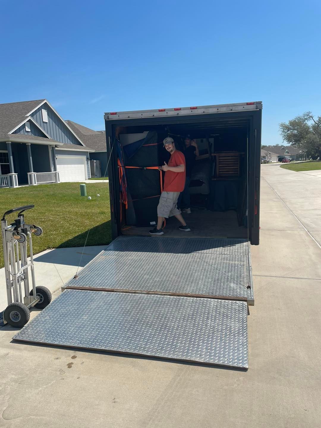 A person standing in the open doorway of a cargo container, loading equipment. A metal ramp extends to the ground.