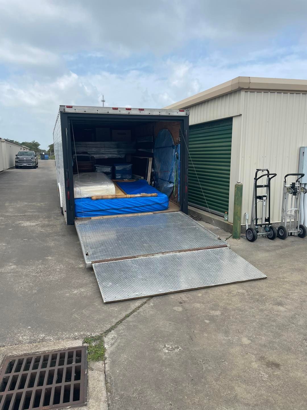 A trailer open with a ramp, loaded with mattresses, next to a storage unit.
